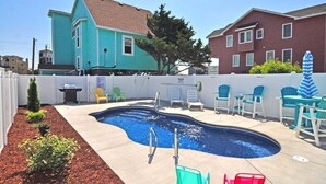 A swimming pool with a diving board, surrounded by a white fence, and adjacent to a house with a red roof.