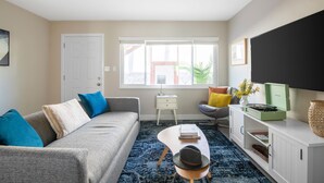 A modern living room with a grey sofa, a coffee table, a TV, and a window with a view of the outside.