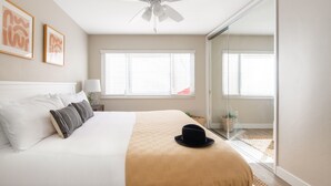 A bedroom with a bed, a ceiling fan, two windows, a sliding glass door, and a black hat on the bed.