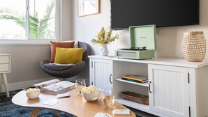 A living room with a comfortable chair, a coffee table with snacks and drinks, a flat-screen TV, and a bookshelf.