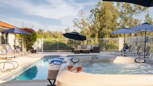 Ein Pool mit Liegestühlen und Sonnenschirmen, ein Whirlpool mit zwei Weingläsern und eine umzäunte Terrasse.