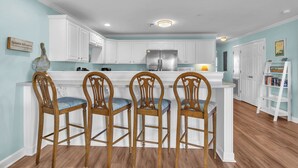 Una cocina con armarios blancos, un refrigerador de acero inoxidable y tres taburetes de madera para barra.