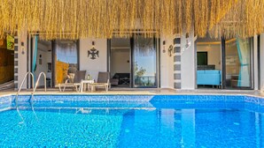 Une piscine à l’eau cristalline, un toit de chaume et un espace détente avec des chaises et une table.