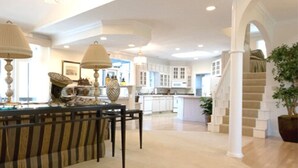 Une cuisine spacieuse avec des meubles blancs, un coin repas avec des chaises à rayures et un escalier menant à un autre niveau.