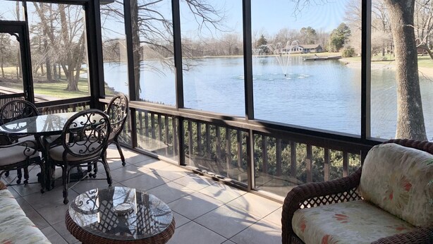 Un espace extérieur abrité, équipé d’une table et de chaises, d’un canapé en osier et offrant une vue sur un lac.
