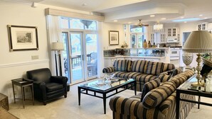 Un salon spacieux avec un grand canapé d’angle, un fauteuil noir et une table basse. Une porte-fenêtre coulissante donne accès à un balcon.
