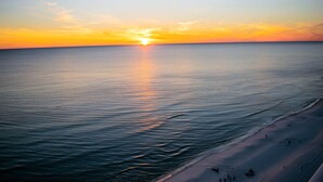 Ein Strand bei Sonnenuntergang mit ruhigem Wasser und wolkenlosem Himmel.