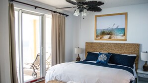 Ein Schlafzimmer mit einem großen Bett, einem Deckenventilator, einer Korbsitzbank, Blick auf den Strand und einem Kinderwagen vor der Schiebetür.