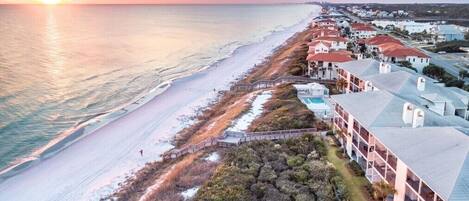 A coastal hotel with a long beachfront, a swimming pool, and a boardwalk leading to the beach.