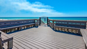 Une jetée en bois qui mène à une plage, avec un ciel bleu dégagé.