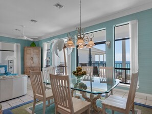 Enjoy meals in this dining area with a glass-top table and six chairs, overlooking the ocean from a large window and balcony.