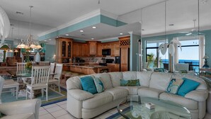 A spacious living area with a large L-shaped sofa, a glass coffee table, and a dining area with a white table and chairs. - Gulf Front, Gorgeous Views, Top Floor, Pool, Gated Complex, 30A (Santa Rosa Beach)