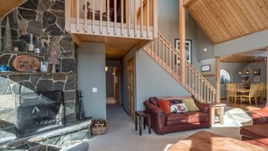 A cozy living room with a stone fireplace, a brown leather sofa, and a wooden staircase. - Beautiful Mountain Home - Next to Sunday River (Newry)