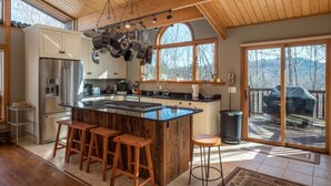 A kitchen with a large island, wooden bar stools, stainless steel appliances, and a view of the outdoors. - Beautiful Mountain Home - Next to Sunday River (Newry)