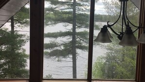 Une pièce dotée d’une grande fenêtre donnant sur une forêt et un plan d’eau. On peut y apercevoir trois luminaires suspendus.