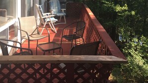 Une terrasse extérieure couverte, dotée d’une table et de chaises, qui offre une vue sur une zone boisée.