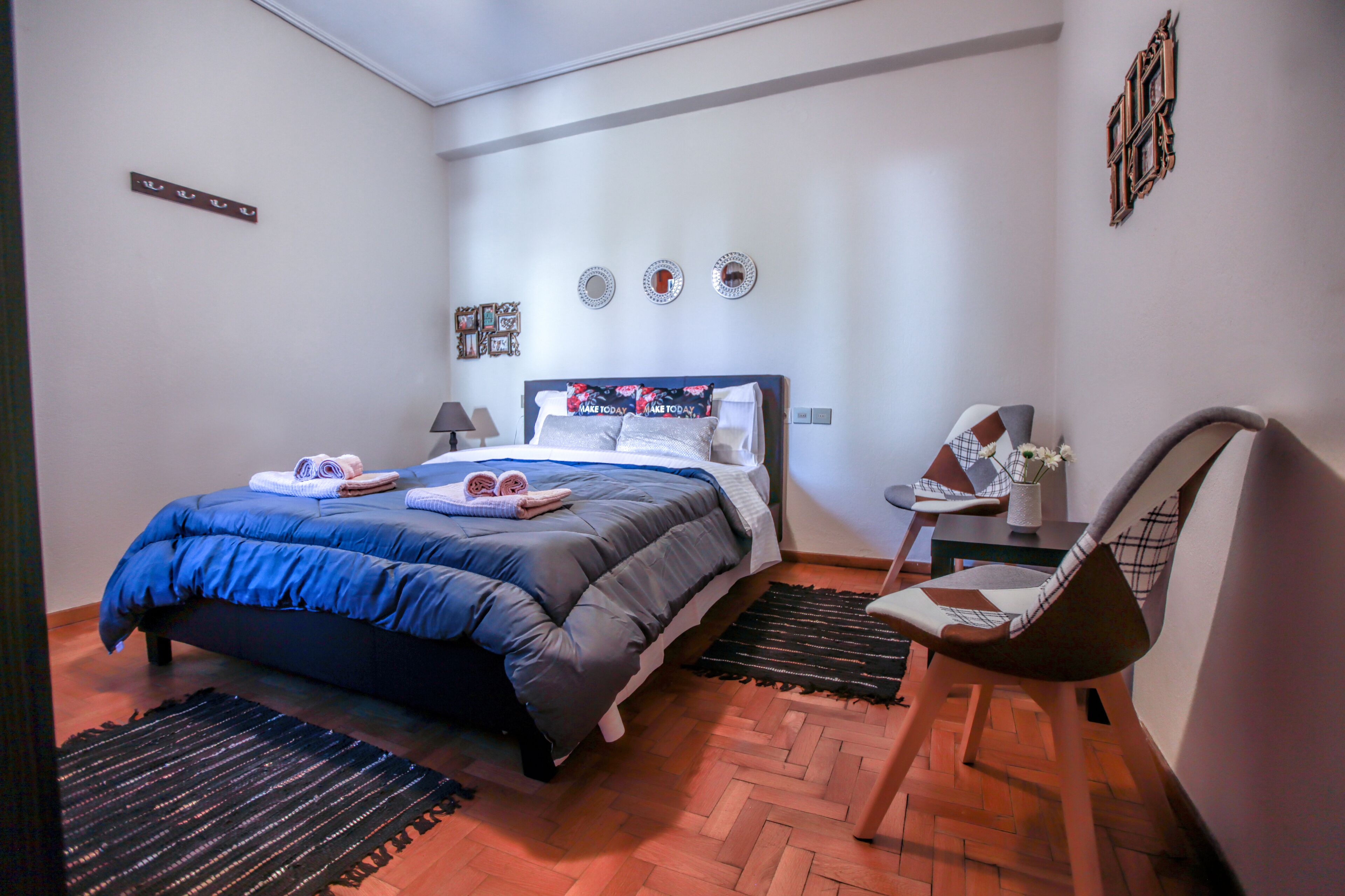 Ein Schlafzimmer mit einem Bett, einem Sessel, einem kleinen Tisch und einem an der Wand befestigten Spiegel.