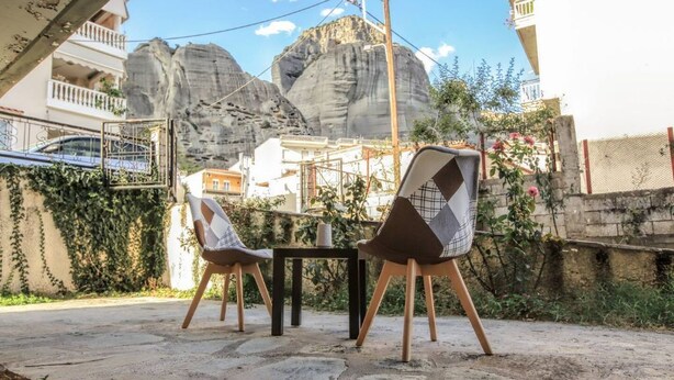 Un espace extérieur aménagé avec deux chaises et une table, entouré d’une terrasse en pierre et offrant une vue sur des falaises rocheuses.