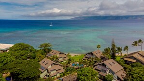A coastal residential area with houses featuring solar panels, a clear view of the ocean, and a distant sailboat. - Spectacular, fully renovated 3-Bedroom Oceanfront Townhome in Kahana (Lahaina)