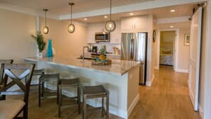 A modern kitchen with a central island, bar stools, hanging pendant lights, and stainless steel appliances. - Spectacular, fully renovated 3-Bedroom Oceanfront Townhome in Kahana (Lahaina)