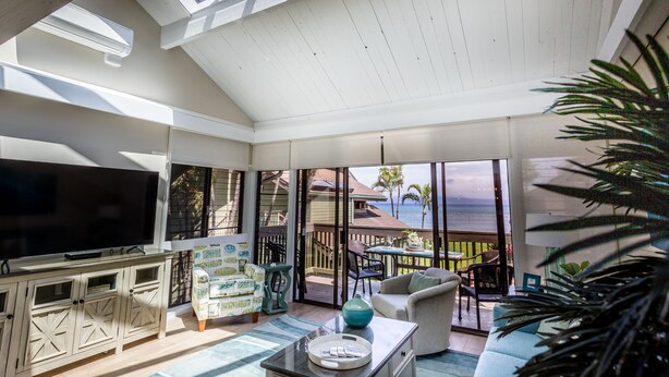 A spacious living room with a large TV, comfortable seating, and a view of the ocean. - Spectacular, fully renovated 3-Bedroom Oceanfront Townhome in Kahana (Lahaina)