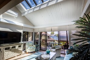 A spacious living room with a large TV, comfortable seating, and a view of the ocean. - Spectacular, fully renovated 3-Bedroom Oceanfront Townhome in Kahana (Lahaina)