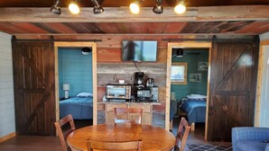 Una habitación de estilo cabaña rústica con una mesa de comedor de madera, sillas, kitchenette con estufa y dos camas con ropa de cama azul.