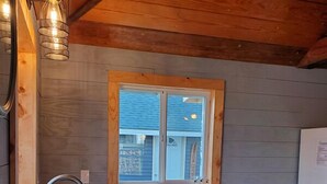 Una cocina con gabinetes de madera, un lavamanos de acero inoxidable, una ventana con persianas y una estufa a gas.