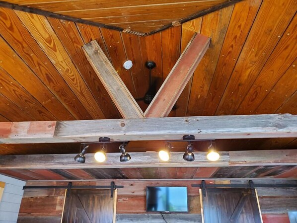 Een rustiek houten plafond met zichtbare balken en vier aan de muur bevestigde lampen.