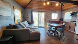 Interior acogedor de una cabaña con sofá, mesa de comedor, sillas y zona de cocina.