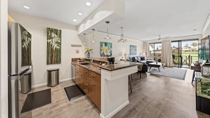 A modern kitchen with a central island, stainless steel appliances, and a dining area with a view. - 2BR/2BA Wailea Condo w AC Pool Close to Beach - Grand Champions 163 (Kihei)