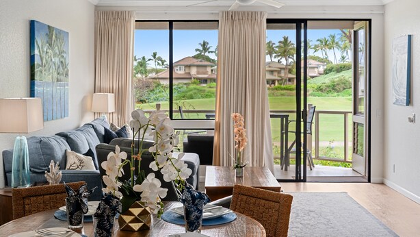 A modern living room with a large window, a ceiling fan, and a dining area with a table set for two. - 2BR/2BA Wailea Condo w AC Pool Close to Beach - Grand Champions 163 (Kihei)