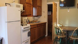 Una cocina compacta con armarios de madera, una estufa blanca, un microondas y una zona de comedor con mesa y sillas.
