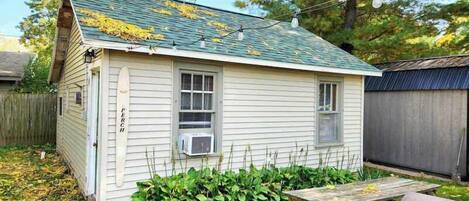 A small, single-story house with a green roof, a small porch, and a wooden fence in the background.