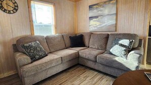 A corner sectional sofa with patterned cushions, a clock on the wall, and a painting above. - Crappie Cabin - Fremont, WI (Fremont)