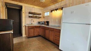 A kitchen with wooden cabinets, a white refrigerator, a microwave, and a sink. - Crappie Cabin - Fremont, WI (Fremont)