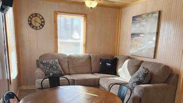 A cozy living room with a wooden ceiling, a round wooden table with chairs, a beige sectional sofa, and a clock on the wall. - Crappie Cabin - Fremont, WI (Fremont)