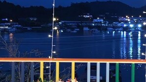 A balcony with a view of a marina at dusk, featuring a railing with lights, a potted plant, and a clear view of boats and buildings across the water. - La Martinera Avenida San José (Guatapé)