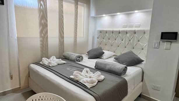 A modern hotel room with a neatly made bed, a flat-screen TV, and a window with sheer curtains. - La Martinera Avenida San José (Guatapé)