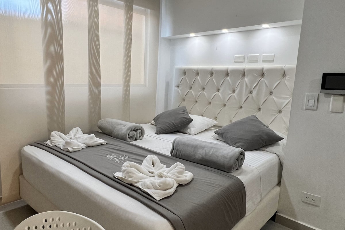 Een moderne hotelkamer met een net opgemaakt bed, een flatscreen televisie en een raam met dunne gordijnen.