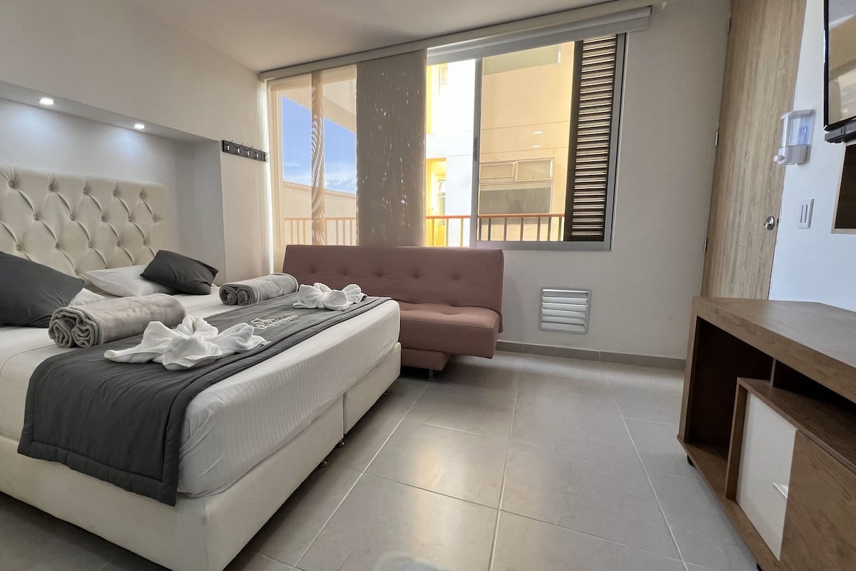 Een moderne slaapkamer met een groot bed, een nachtkastje, een kleine bank en een raam met zonwering.