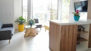 A modern living room with a sofa, a coffee table, and a wooden island. There is a TV mounted on the wall and a balcony with a view. - La Martinera Avenida San José (Guatapé)