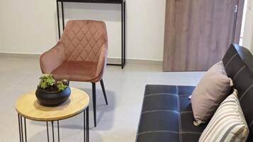 Een moderne woonkamer met een zwarte bank, een bruine fauteuil, een ronde salontafel met een plant, een spiegel aan de muur en een houten deur met het nummer 404.