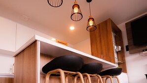 A modern kitchen with wooden cabinets, a central island with stools, pendant lighting, and a flat-screen TV mounted on the wall. - La Martinera Avenida San José (Guatapé)