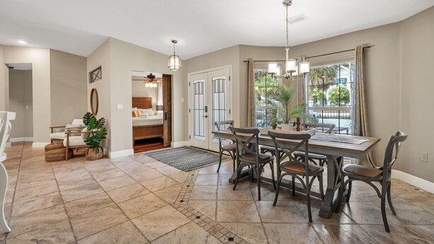 A spacious dining area with a large wooden table and six chairs, a small side table with a vase, and a view of the outdoors through a large window. - Double oven | Volleyball Net | 4 Famous Beaches | 1 Level (Sarasota)