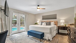 A bedroom with a bed, a bench, a TV, a ceiling fan, a nightstand, and a view of a pool through glass doors. - Double oven | Volleyball Net | 4 Famous Beaches | 1 Level (Sarasota)