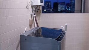 A compact, modern bathroom with a built-in washer and dryer, white tiled walls, and a window with a cityscape view. - Sunny Private Apt of Grand Continental (Guangzhou)