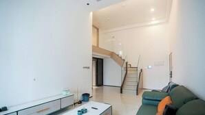 A modern living room with a sofa, a coffee table, and a staircase leading to an upper floor. - Sunny Private Apt of Grand Continental (Guangzhou)