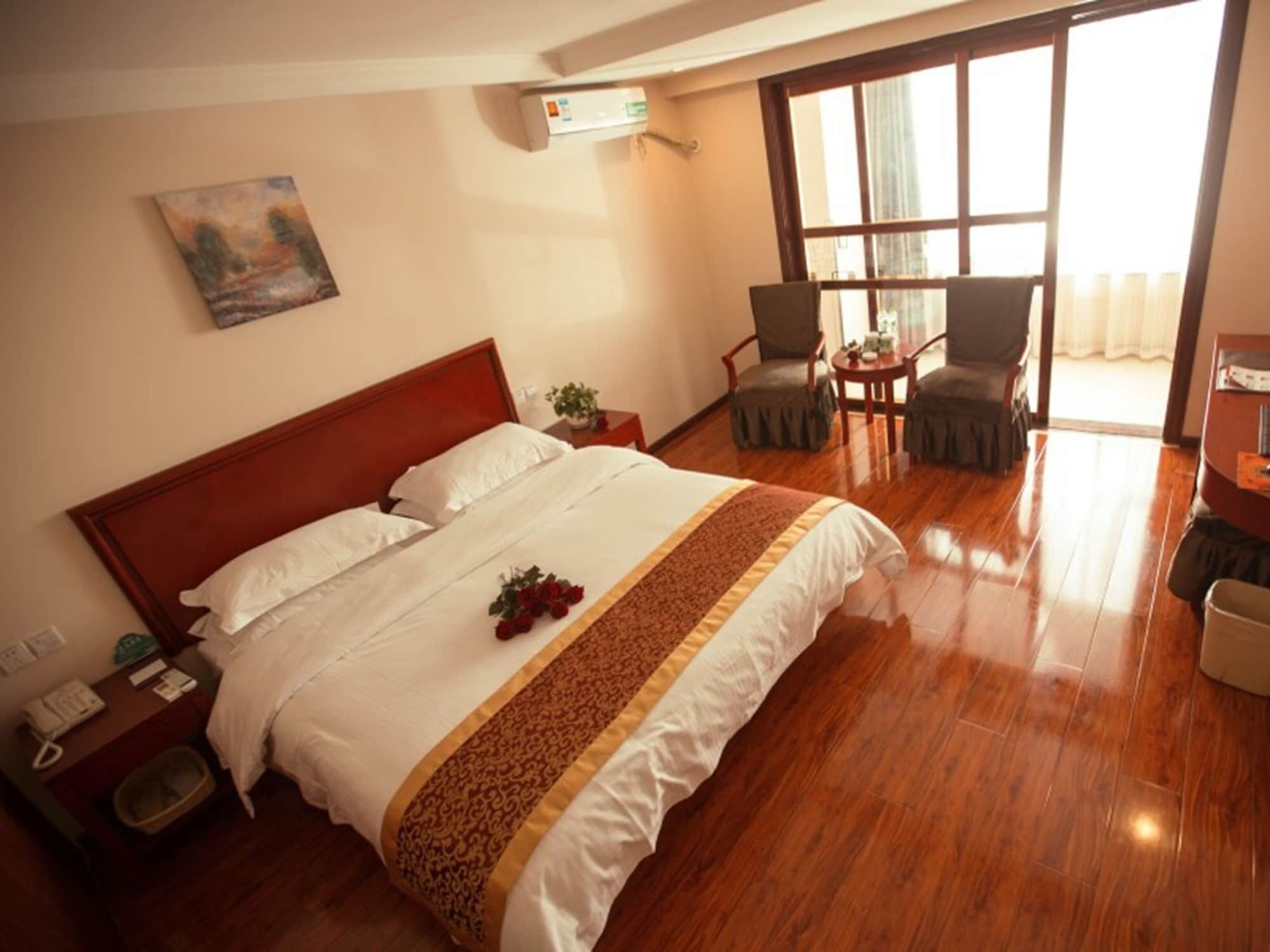 A hotel room with a large bed, a bedside table with a phone, a small table with chairs, and a window with curtains.