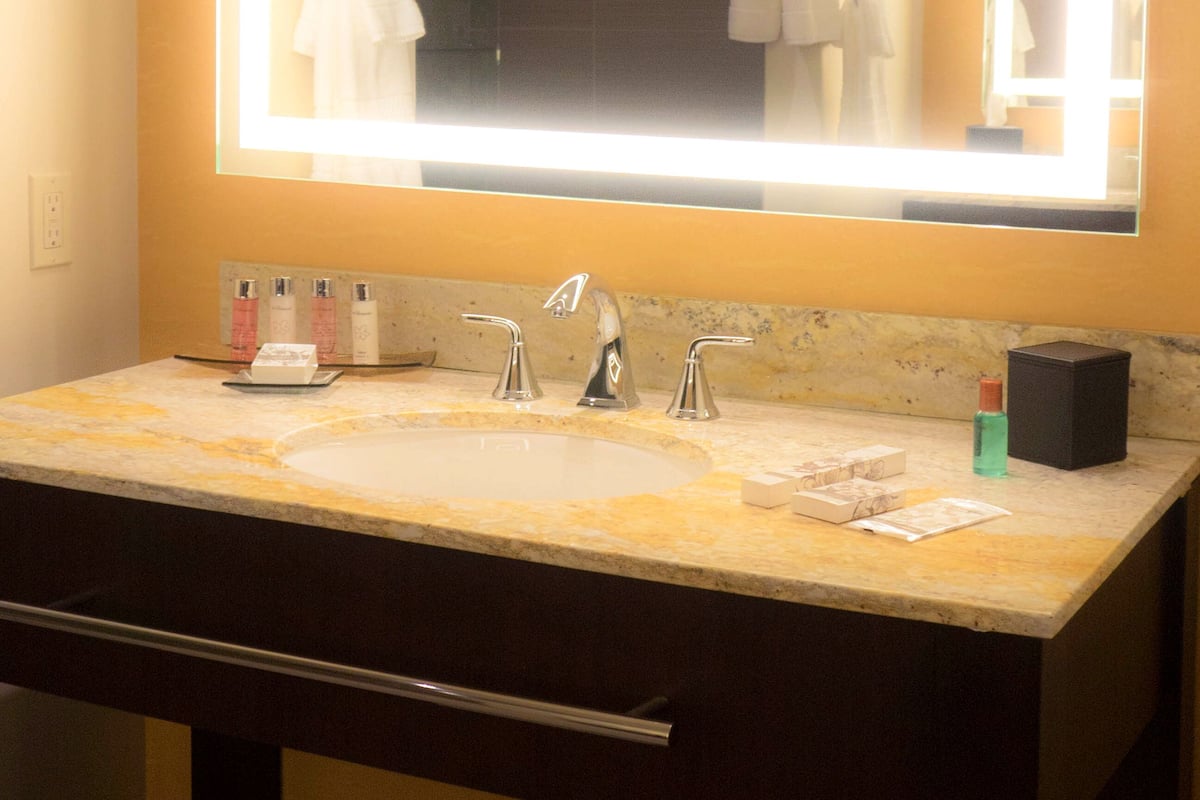 A bathroom with a large mirror, two sinks, and a vanity with toiletries.